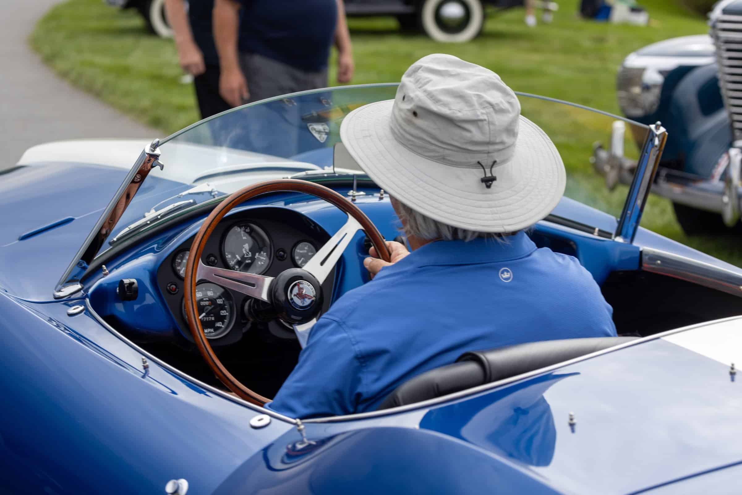 Driver in a blue roadster, wood-rim wheel